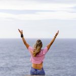 a woman with her arms raised in front of a body of water